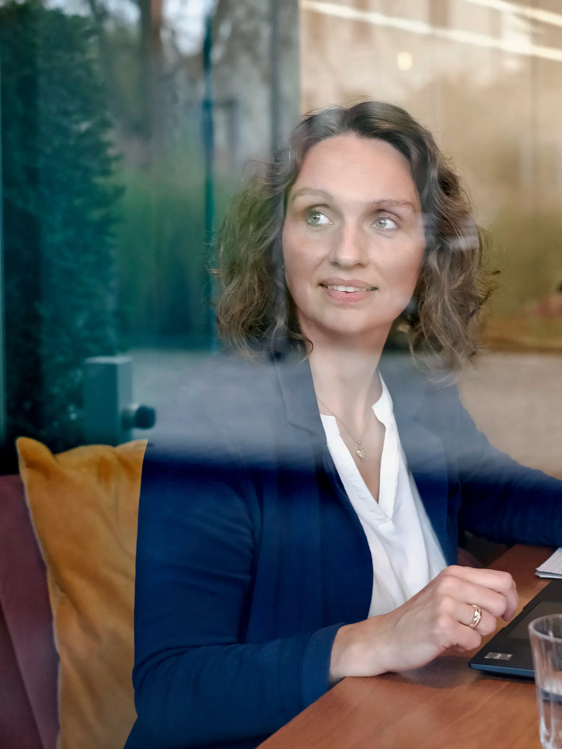 Marion Elsinghorst in einem lässigen dunkelblauen Blazer, scheinbar in einem Coaching-Gespräch in einem Café in Bocholt, blickt inspiriert in die Ferne.